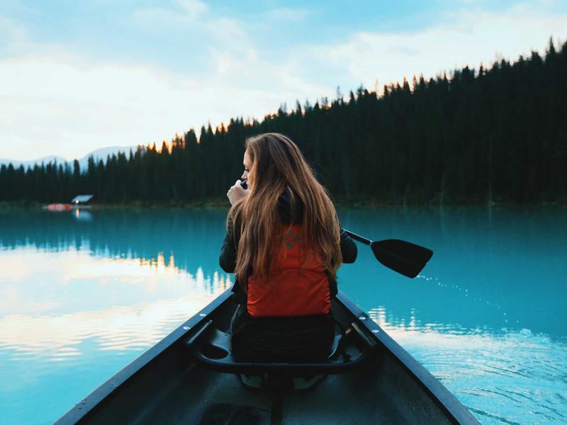 Woman paddling a canoe on a calm turquoise lake with forested shoreline